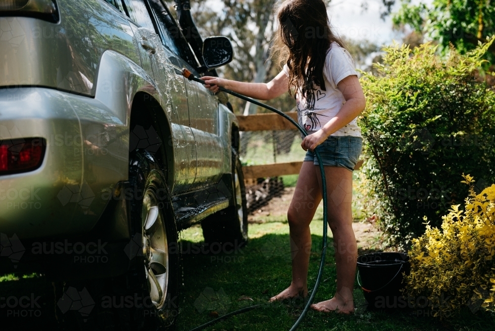 Girl washing a car with a hose - Australian Stock Image