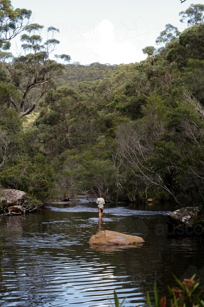 Girl wearing a swimsuit exploring a river by herself - Australian Stock Image