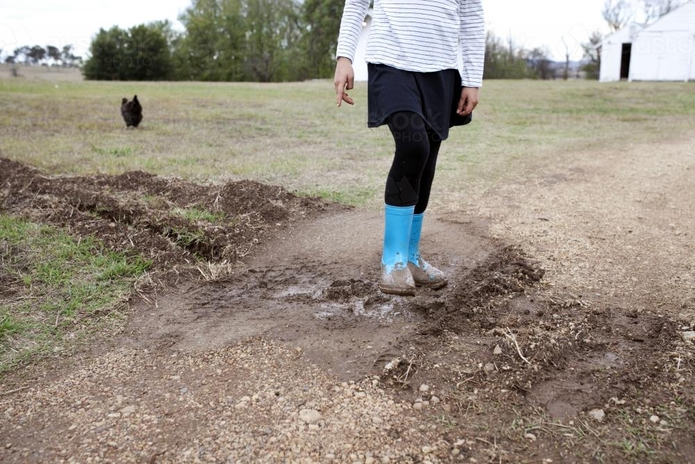 Girl wearing blue gumboots walking across mud on the farm - Australian Stock Image