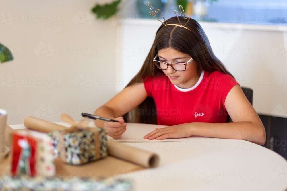 girl wearing sparkly antler headband writing Christmas card - Australian Stock Image