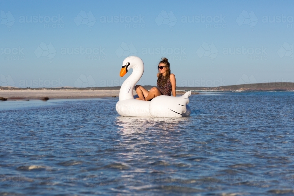 Girl wearing sunglasses and relaxing in an inflatable swan - Australian Stock Image