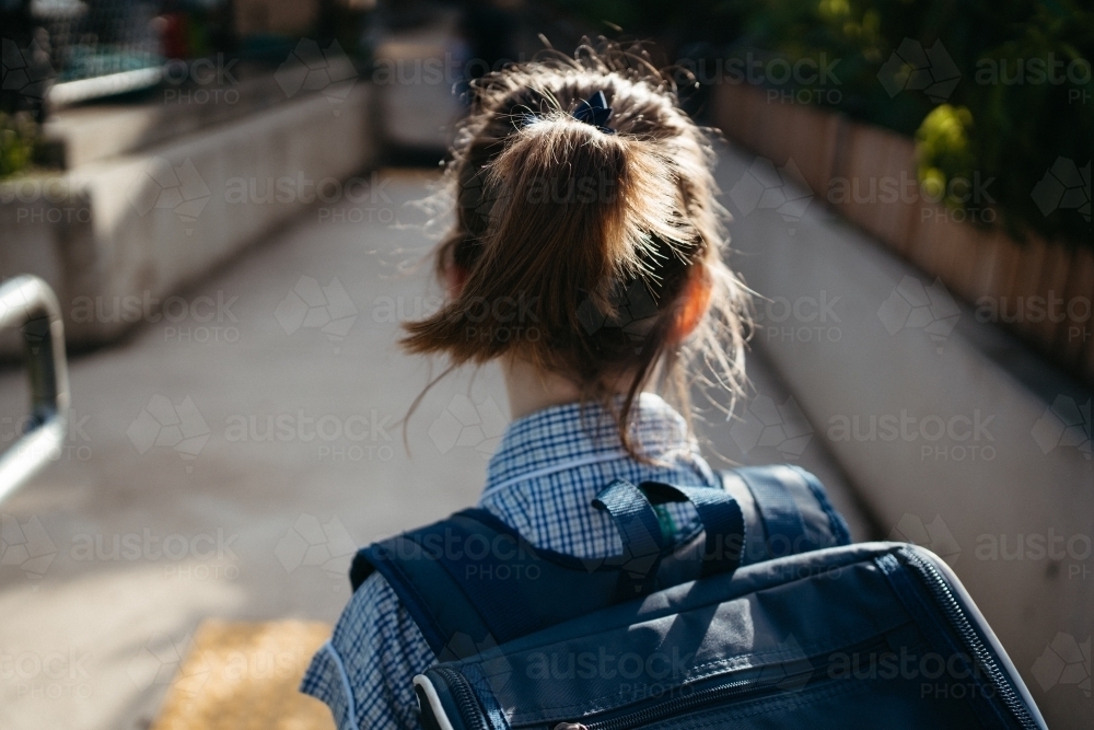 Girl with a ponytail in a school dress with a backpack walks along a path - Australian Stock Image