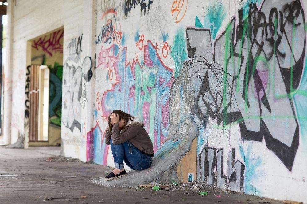 Girl with head in hands and wall of graffiti - Australian Stock Image