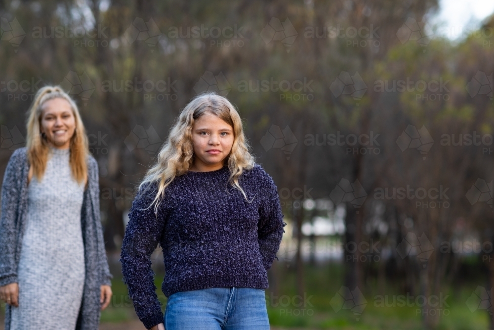 girl with long blonde hair, with mother blurred in background - Australian Stock Image