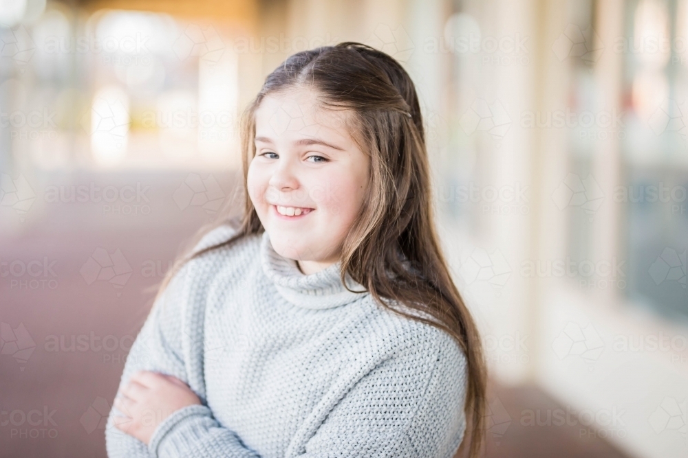 Girl with long hair smiling cheekily with arms crossed - Australian Stock Image