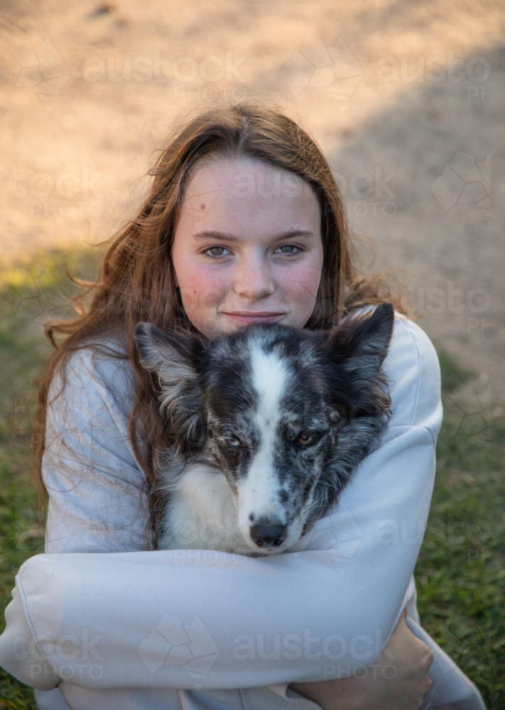 Girl with long hair smiling in portrait and hugging her dog - Australian Stock Image