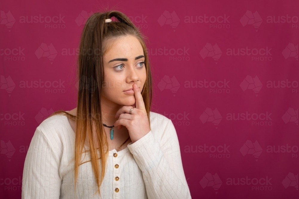 girl with one finger to lips against dark pink background - Australian Stock Image