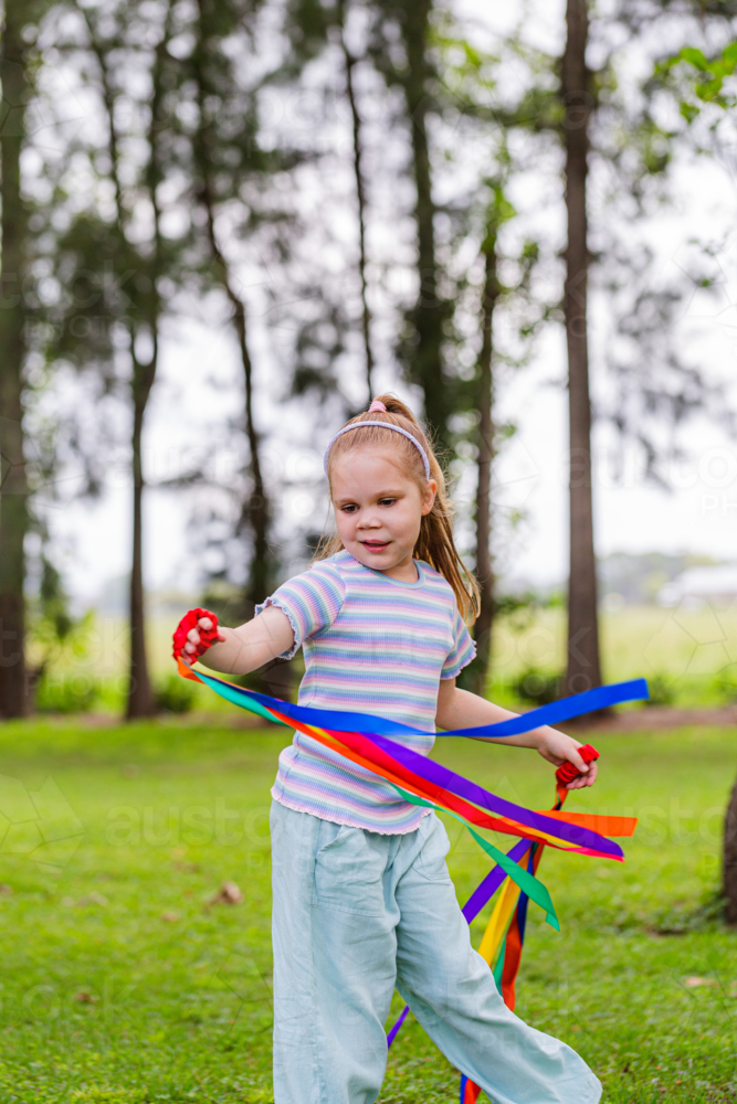 Girl with rainbow streamers running around outside in country - Australian Stock Image