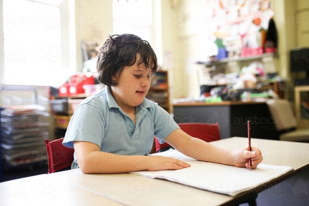girl with short hair wearing pale blue shirt sitting and drawing on the book with pencil - Australian Stock Image