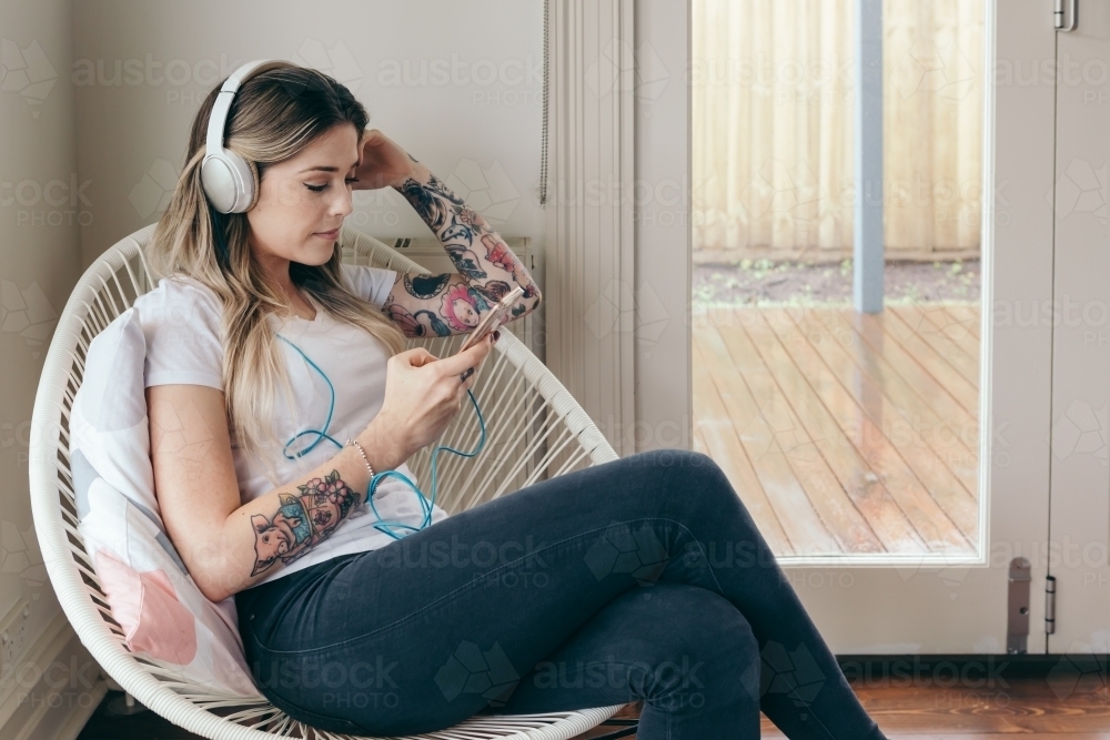 Girl with tattoos creating a playlist on her smart phone - Australian Stock Image