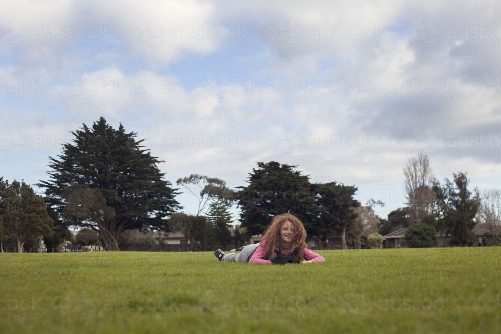 Girl with wild hair lying on short grass in park - Australian Stock Image