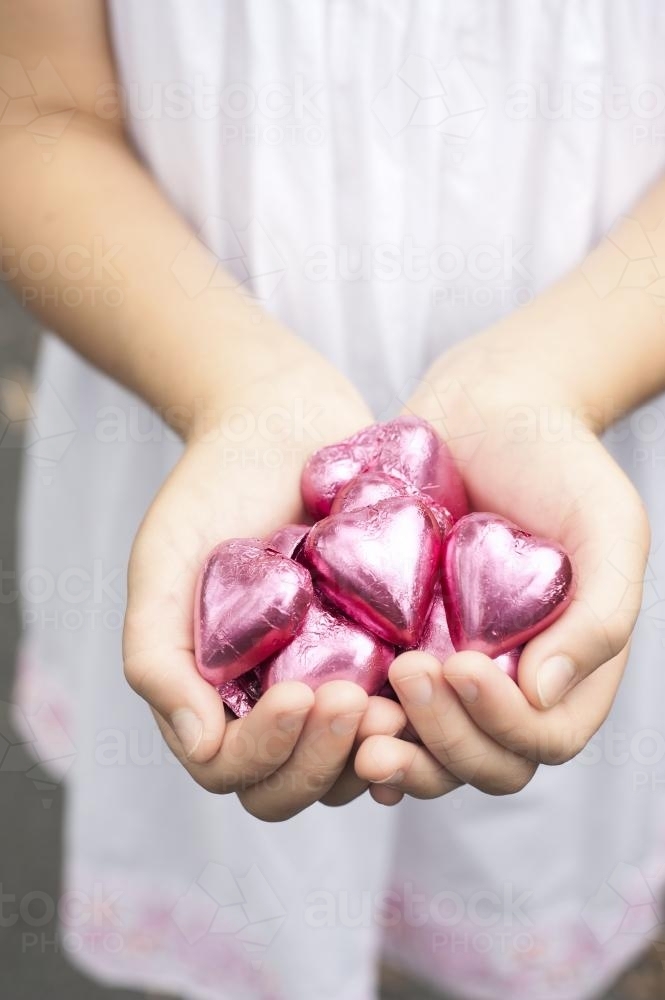 girls hands holding pink chocolate hearts - Australian Stock Image