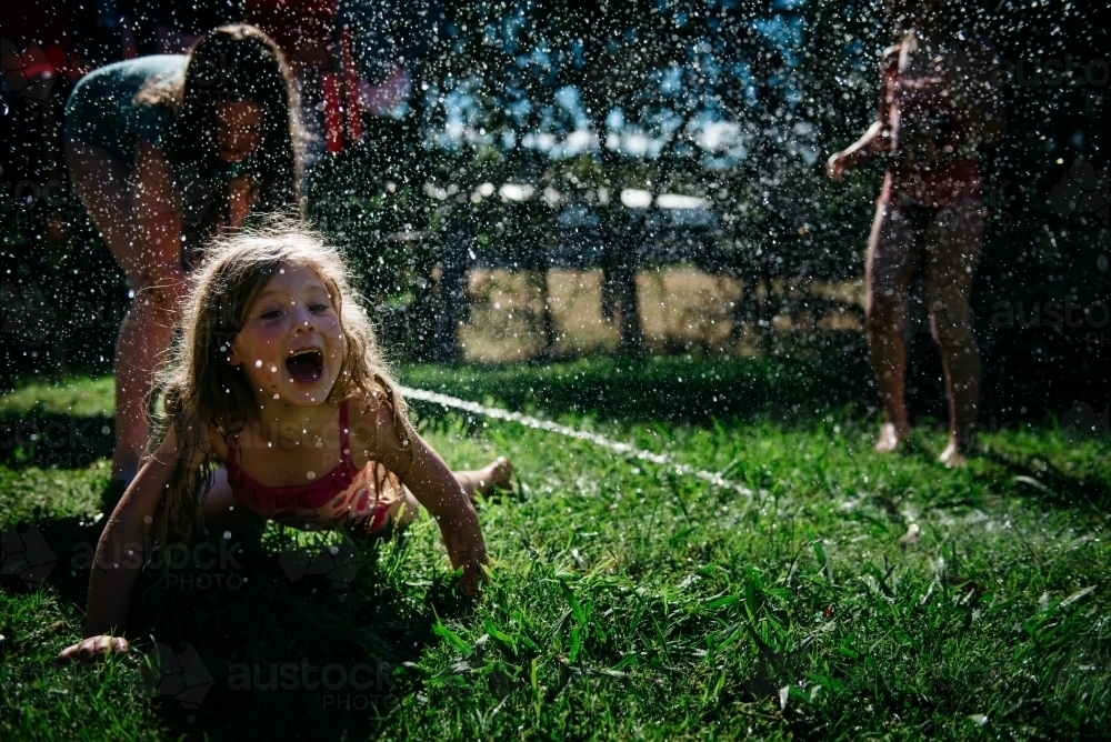 Girls playing under hose, blonde child laughing on ground - Australian Stock Image