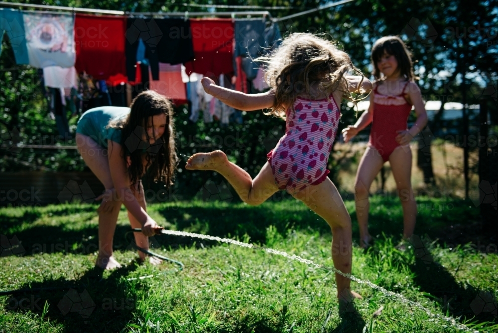 Girls playing under hose, blonde girl jumping over water - Australian Stock Image
