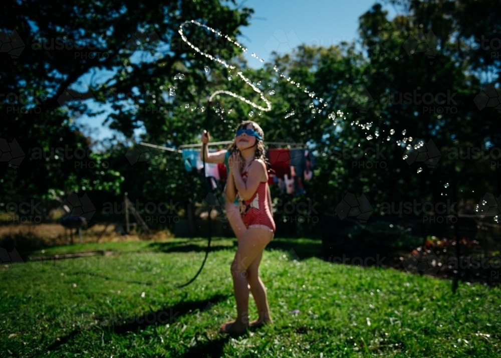 Girls playing under hose, brunette girl looking up, soft focus - Australian Stock Image