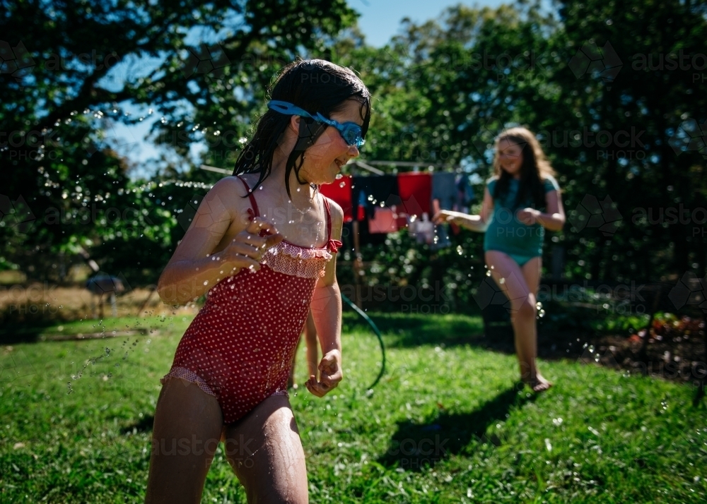 Girls playing under hose, brunette girl running through water - Australian Stock Image