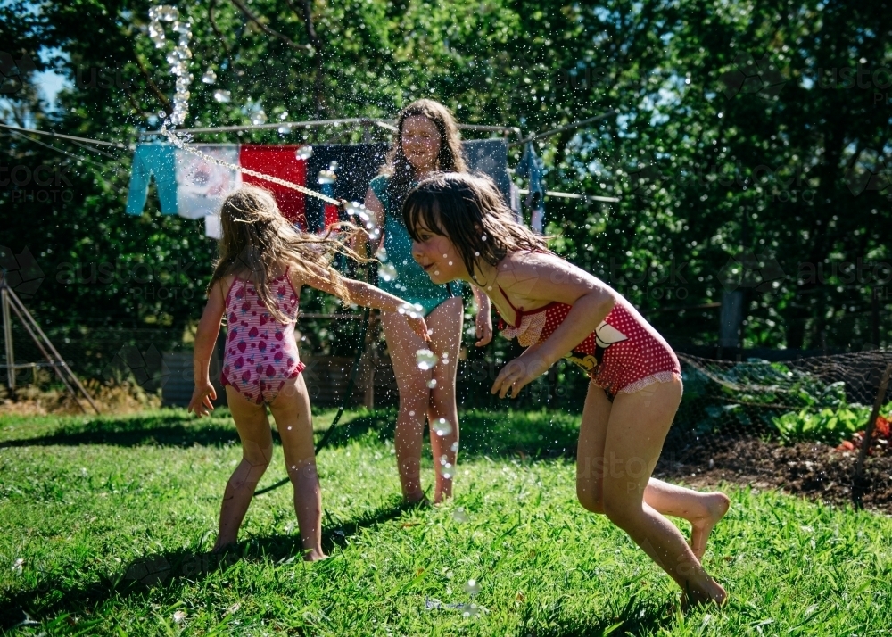 Girls playing under hose, brunette girl running under water - Australian Stock Image