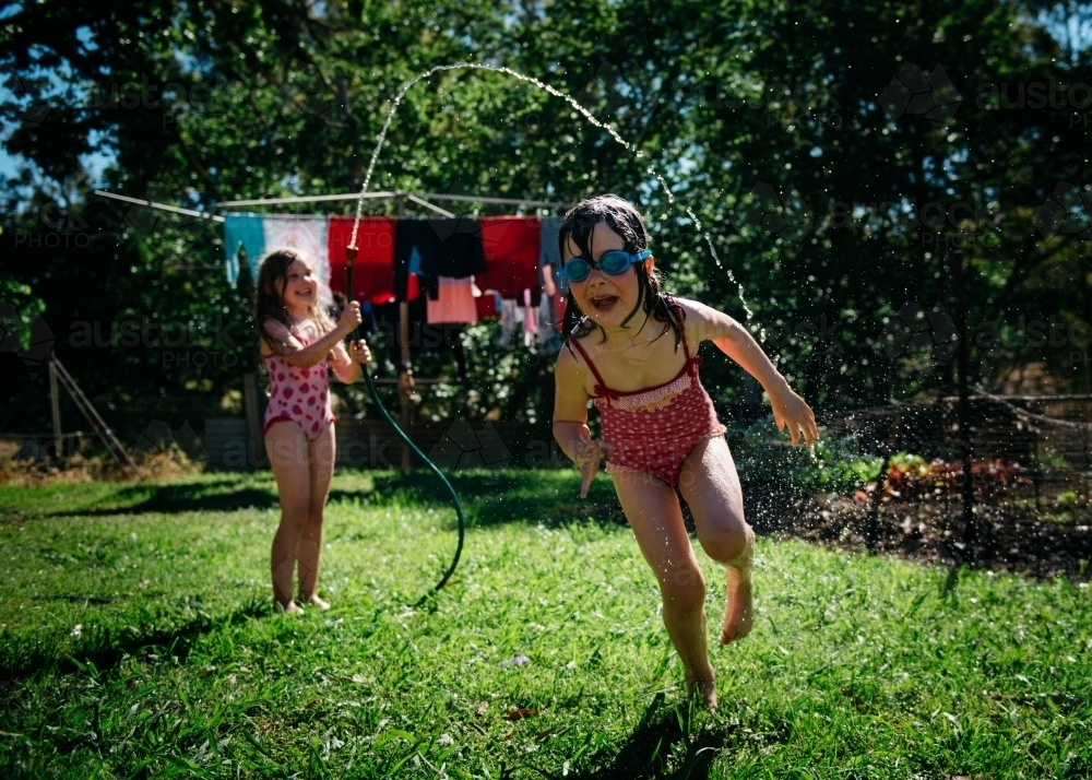 Girls playing under hose, brunette girl running under water with goggles on - Australian Stock Image