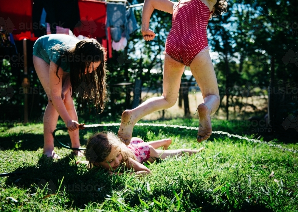 Girls playing under hose, jumping and crawling - Australian Stock Image