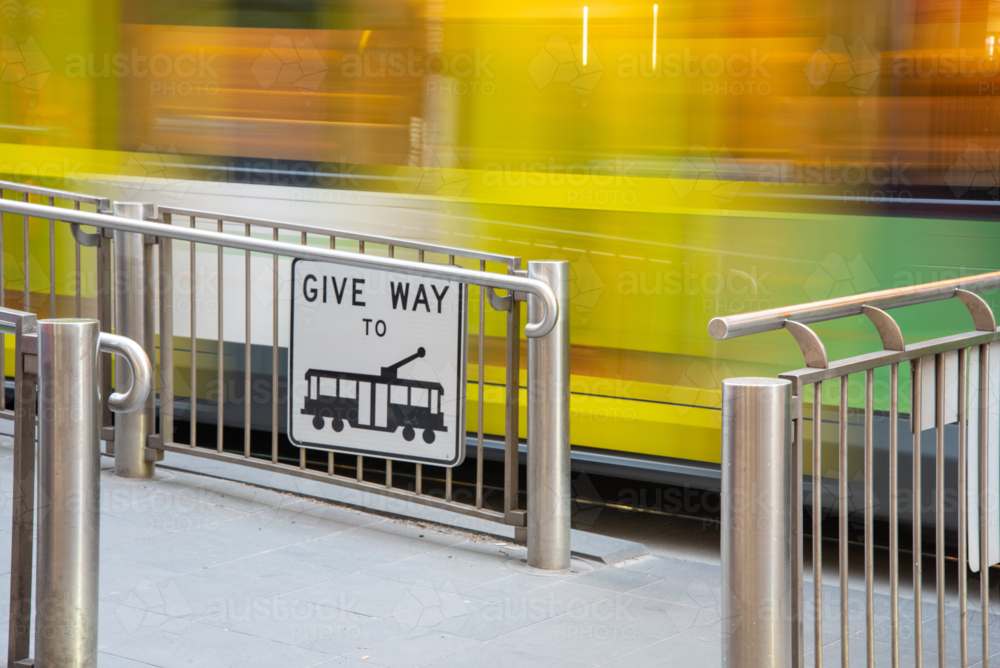 Give way to trams sign at a tram stop with a tram moving past in the background - Australian Stock Image