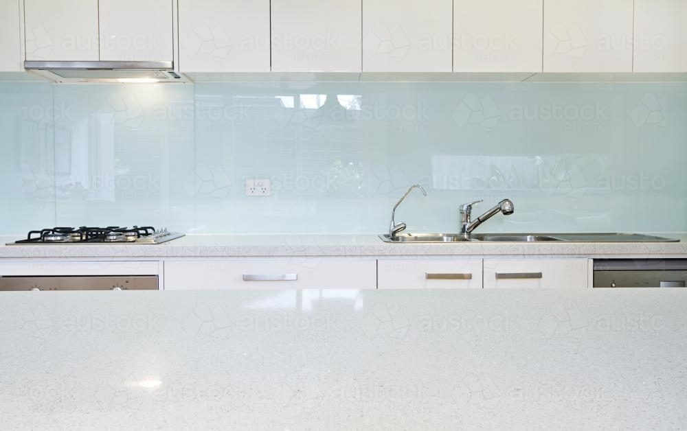 Glass kitchen splashback and white counter tops in designer home - Australian Stock Image