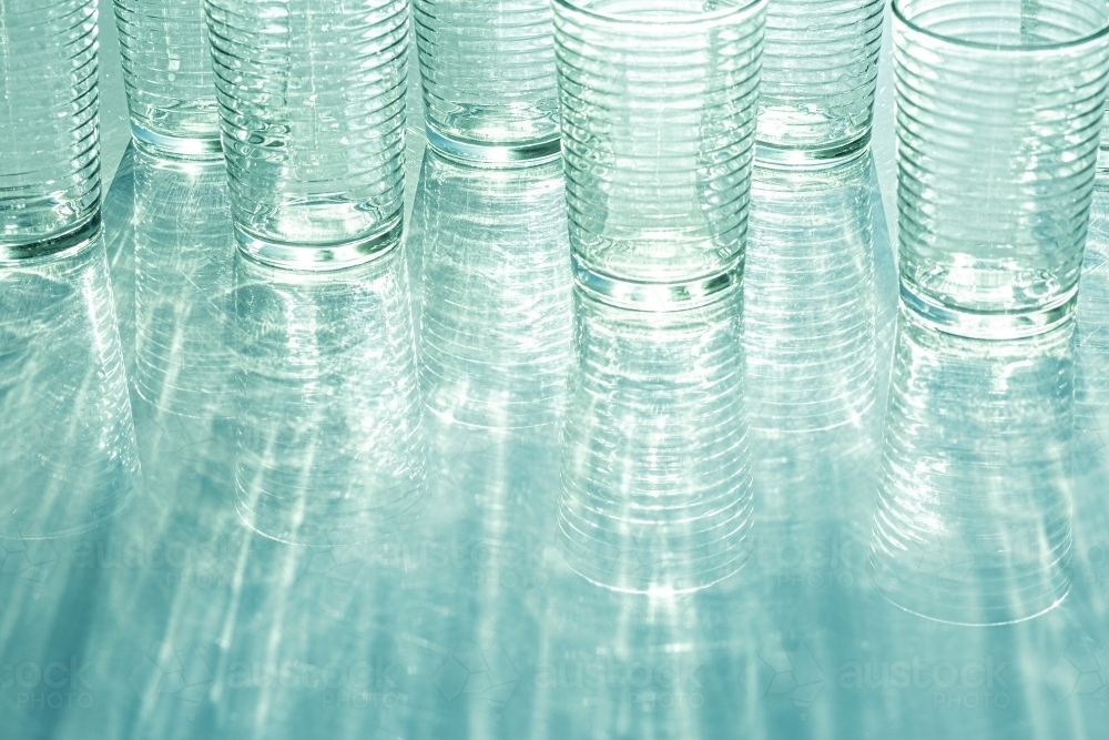 Glasses reflecting turquoise light throwing rippled shadow pattern reflection - Australian Stock Image