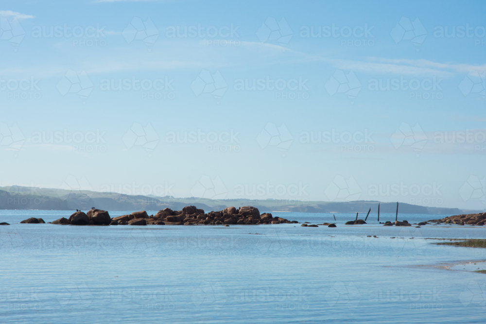 Glassy sea, rocks and old jetty on a sunny day - Australian Stock Image