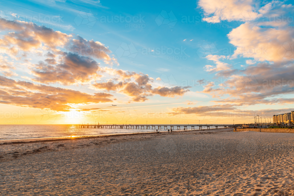 Glenelg Beach with jetty and people walking along the shore during sunset, South Australia - Australian Stock Image