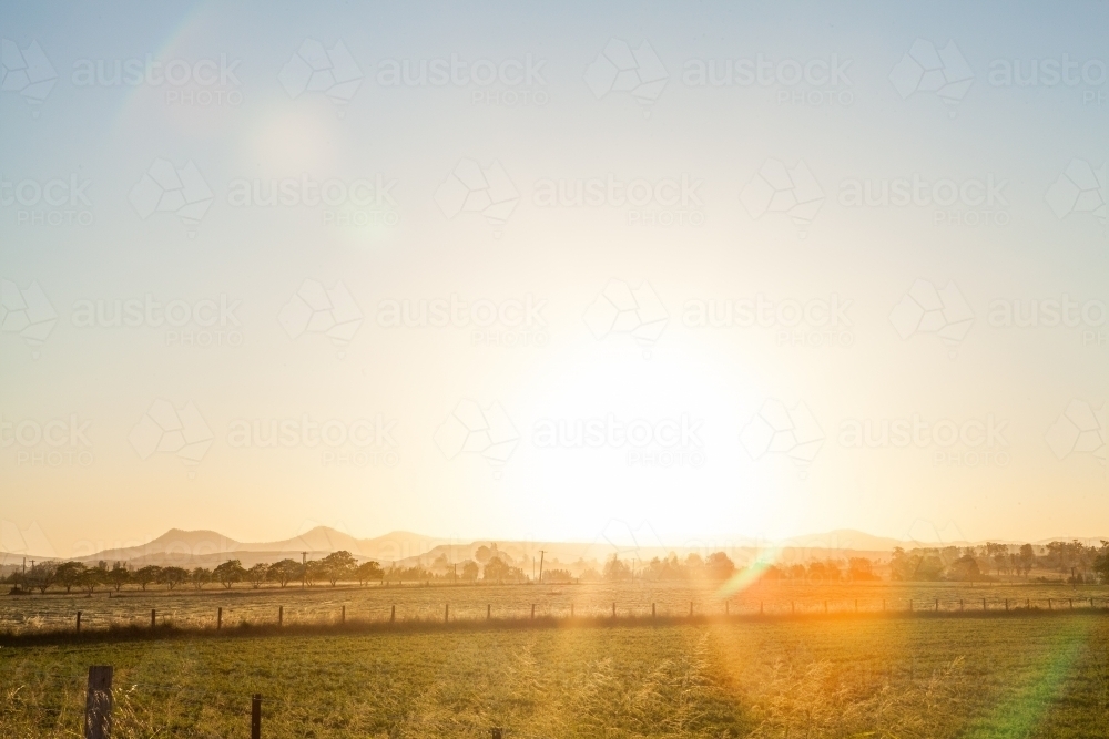 Glow of setting sun shining over farm paddock and Bulga hills - Australian Stock Image