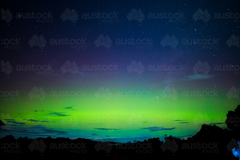 glowing green and blue aurora over dark landscape - Australian Stock Image