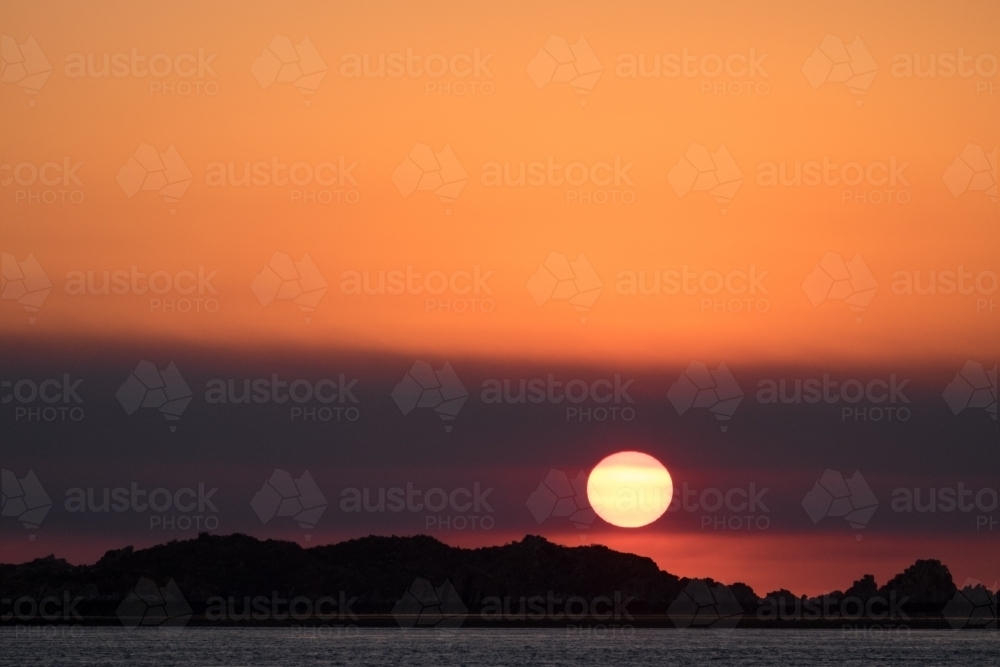Glowing orange sunset with hazy sky over the rocky shore of the Kimberley coast Western Australia - Australian Stock Image
