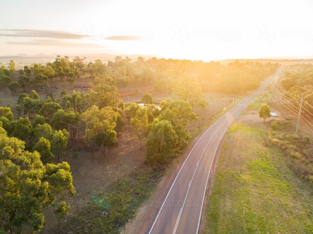 Gold light shining over trees and rural country road - Australian Stock Image