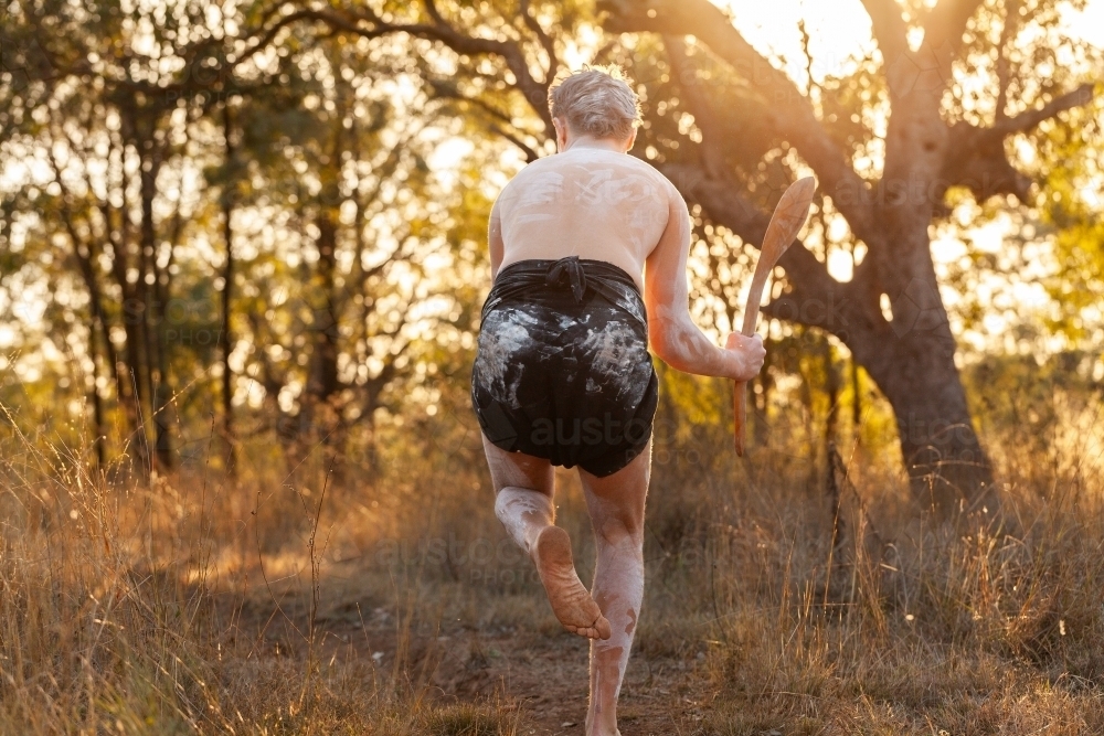 Golden Australian sun behind young First Nations man holding hunting stick in bushland - Australian Stock Image