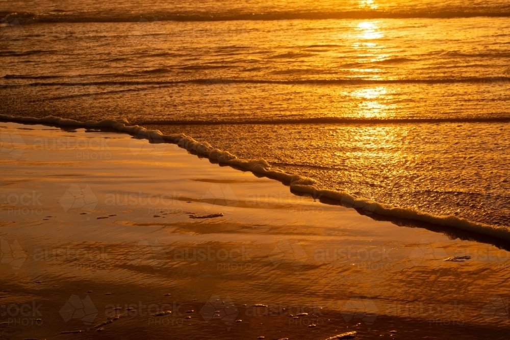 Golden beach scene with edge of the water and reflections - Australian Stock Image