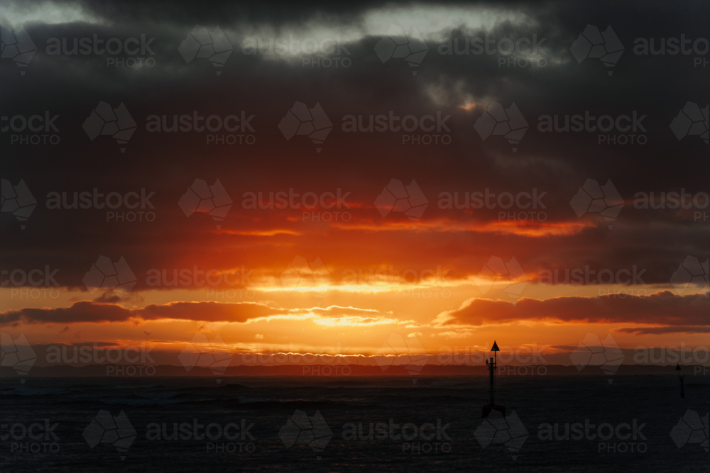 golden coastal sunset partially hidden behind a dense layer of clouds - Australian Stock Image