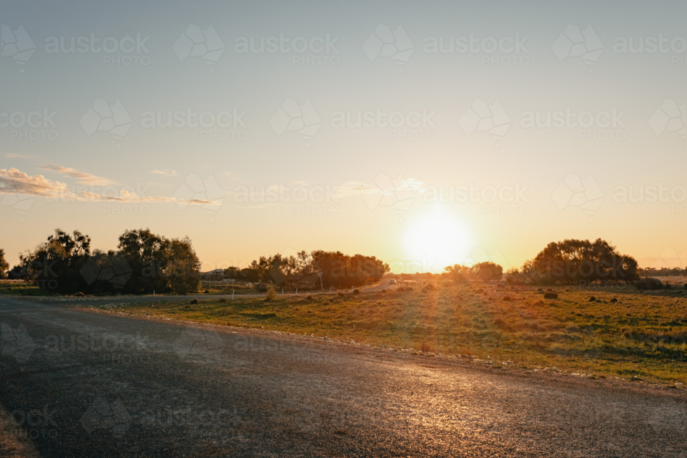 Golden hour sunset over a rural landscape with a bitumen road leading into the distance - Australian Stock Image