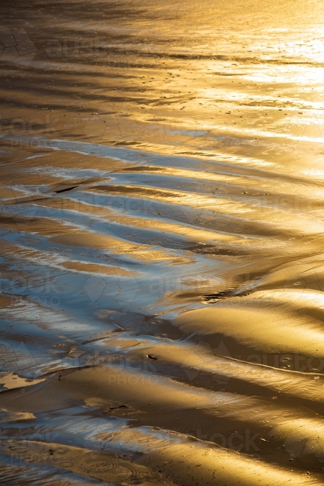 Golden light reflecting off a rippled wet beach - Australian Stock Image