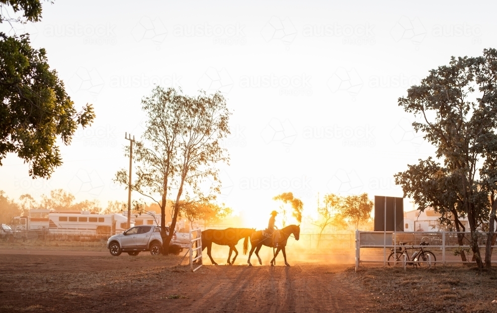 Golden light shining on cowboy riding horse - Australian Stock Image