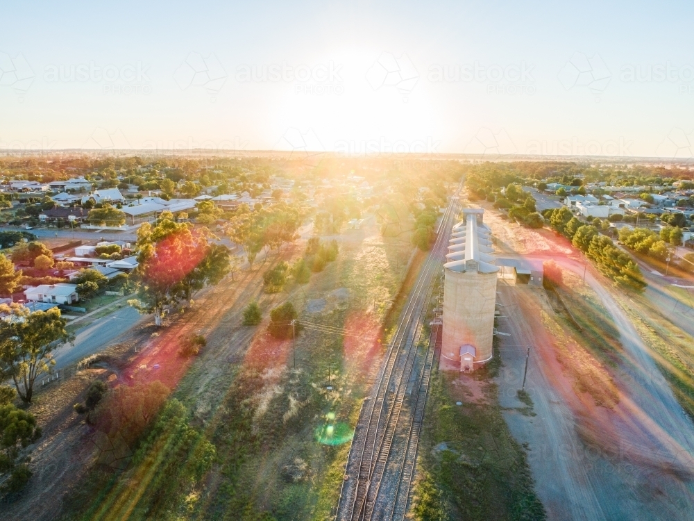 Golden sun flare over landscape aerial view of grain silos beside train line - Australian Stock Image