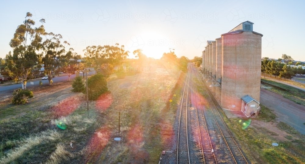 Golden sun flare over landscape aerial view of grain silos beside train line - Australian Stock Image
