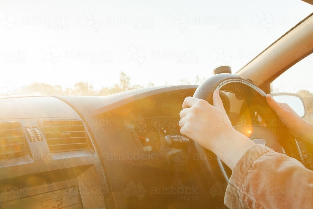 Golden sunlight flare over steering wheel and hands of car driver - Australian Stock Image