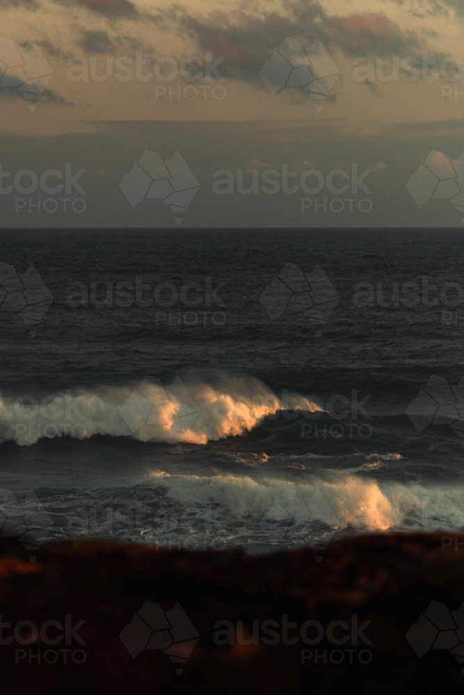 Golden sunlight reflecting on ocean waves at coastline - Australian Stock Image