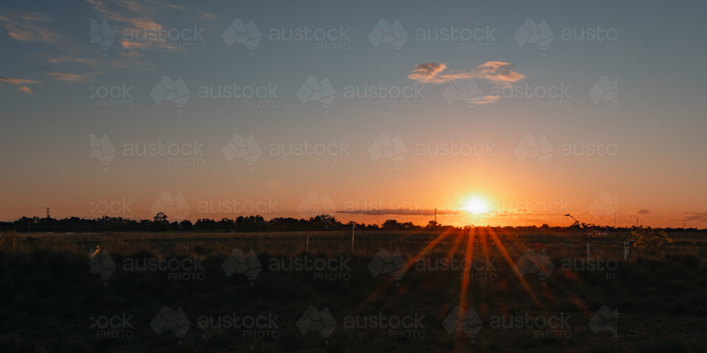 Golden sunset over a rural field with dramatic sunbeams piercing the horizon - Australian Stock Image