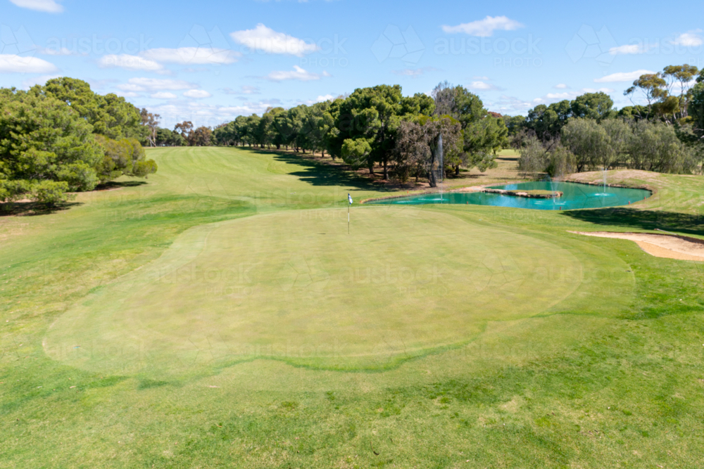 Golf course green and bunkers on a sunny day, surrounded by trees and blue sky - Australian Stock Image