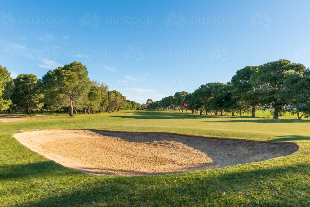 Golf course green and bunkers on a sunny day, surrounded by trees and blue sky - Australian Stock Image