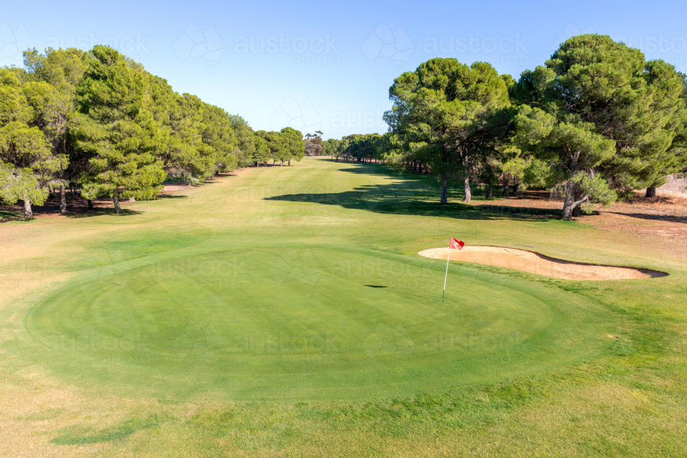 Golf course green and bunkers on a sunny day, surrounded by trees and blue sky - Australian Stock Image