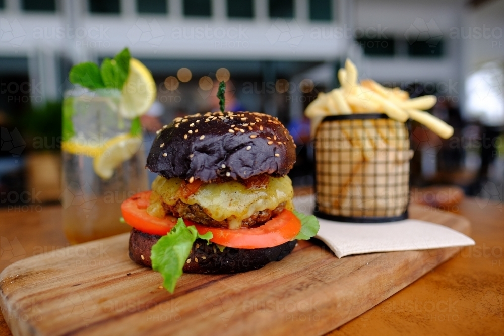 Gourmet burger in black brioche bun served with chips on a platter at a trendy cafe - Australian Stock Image
