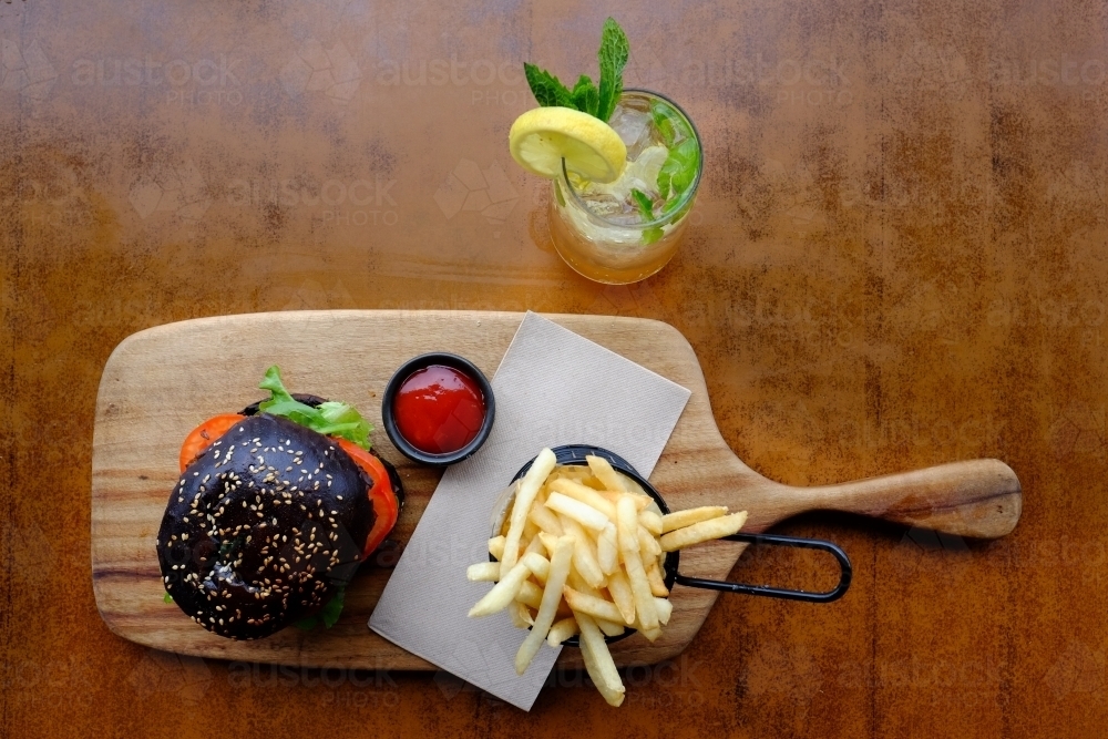 Gourmet burger in black brioche bun served with chips on a platter at a trendy cafe - Australian Stock Image