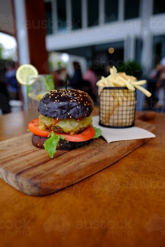 Gourmet burger in black brioche bun served with chips on a platter at a trendy cafe - Australian Stock Image