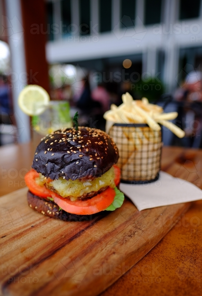Gourmet burger in black brioche bun served with chips on a platter at a trendy cafe - Australian Stock Image